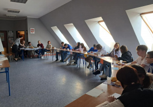 Grupa uczestników w ławkach rozwiązuje zadania