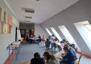 Grupa uczestników w ławkach rozwiązuje zadania