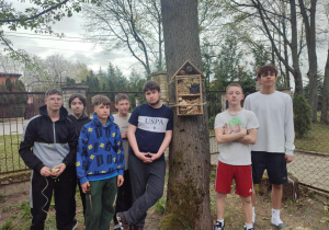Uczniowie pozują do zdjęcia grupowego z jednym z domków na drzewie