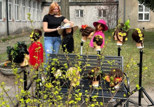 Fryzury na manekinach z wplecionymi kwiatami ustawione na dziedzińcu szkoły
